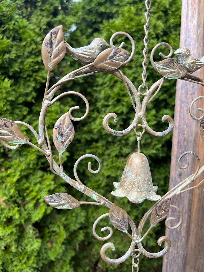 Decorative metal wall hanging with floral and bell design against a green foliage background