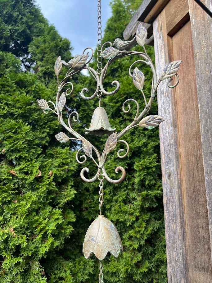Decorative metal wind chime with floral designs hanging against a natural background.