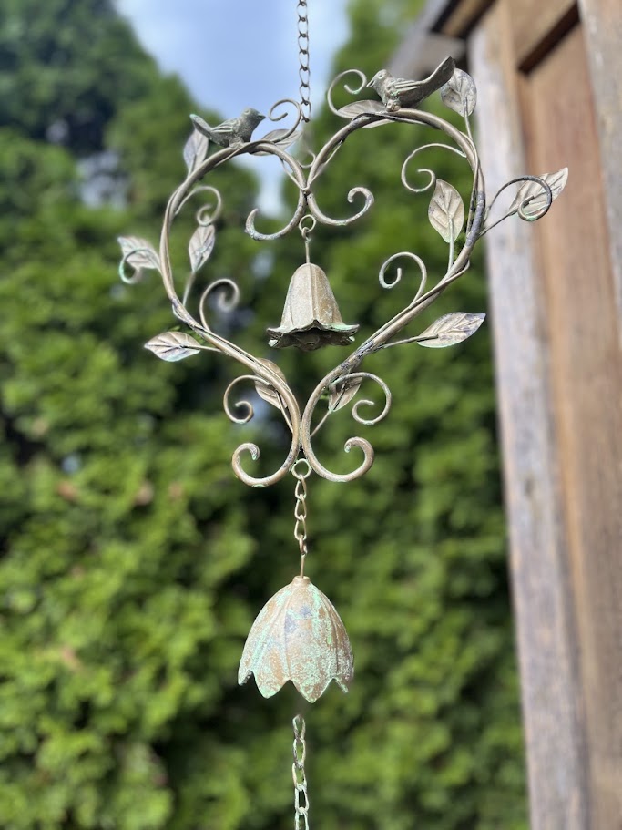 Decorative wind chime with floral design and hanging bell against a blurred green background