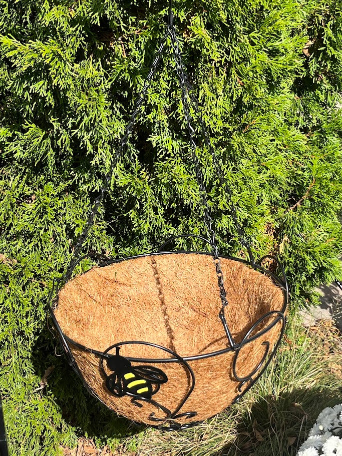 Hanging basket with a black and yellow bee design against a green foliage background