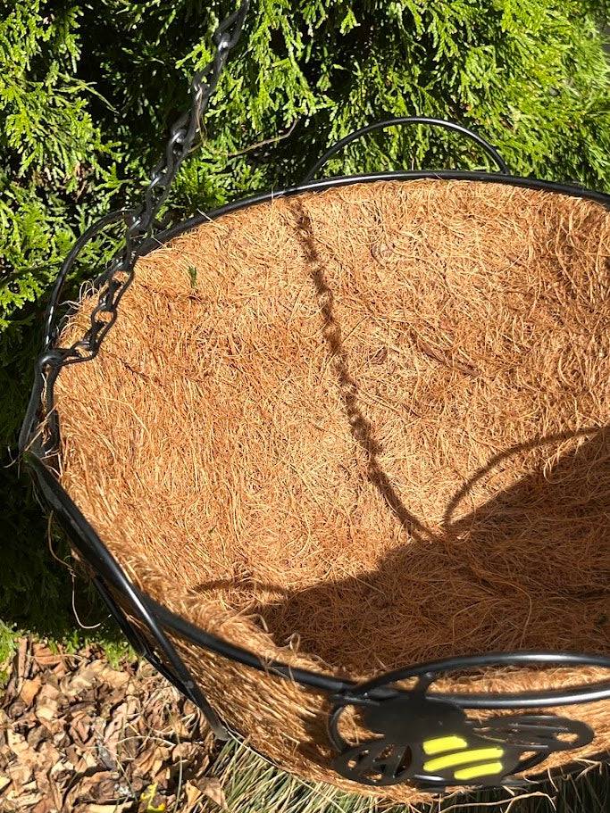 Hanging basket with a black and yellow bee design against a green foliage background