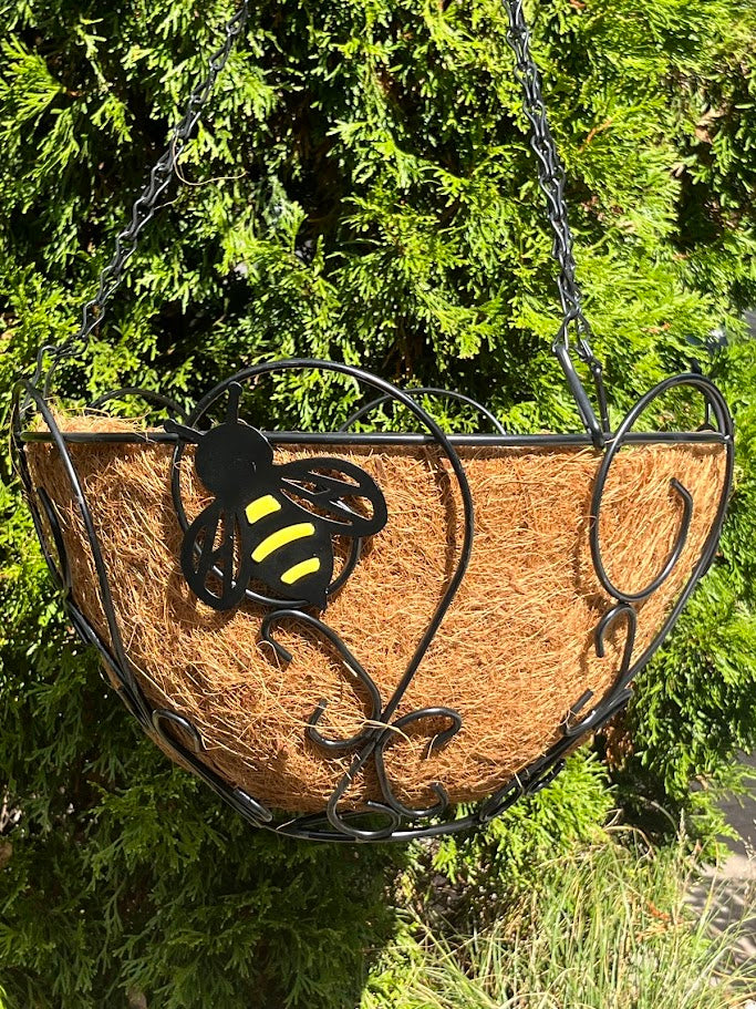 Decorative hanging planter with a bee design against a green foliage background