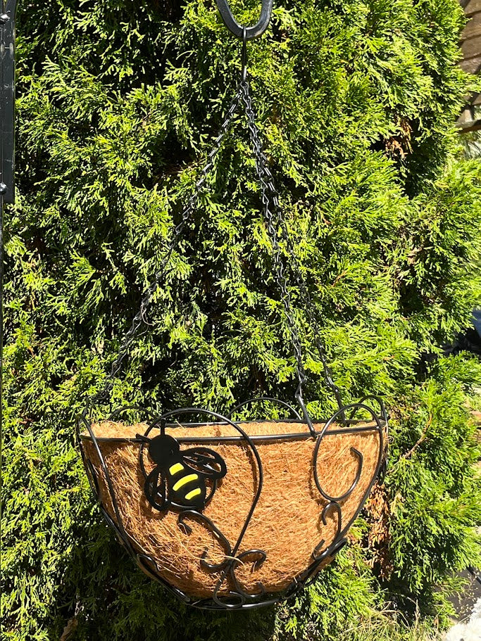 Decorative hanging basket with a bee design against a green leafy background