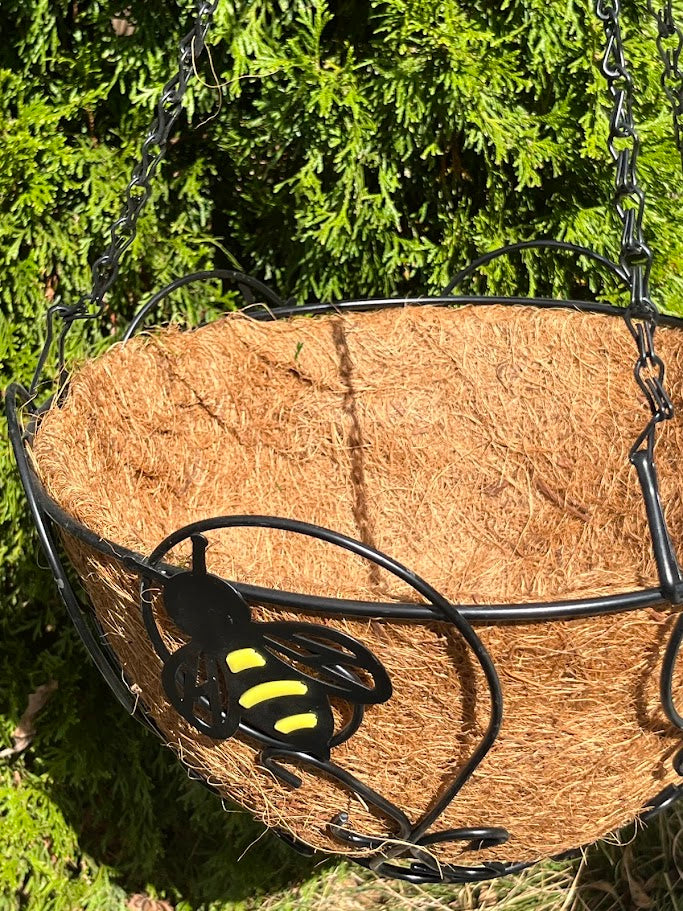 Hanging basket with a black and yellow bee design against a green foliage background