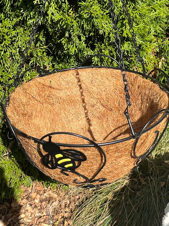 Hanging basket with a black and yellow bee design against a green foliage background