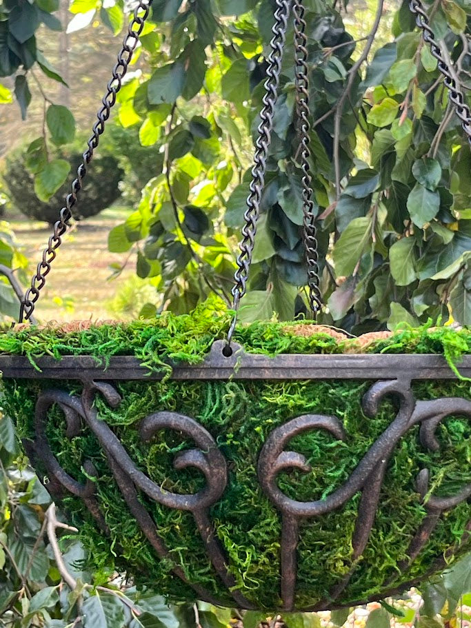 Decorative moss-covered hanging planter with metal hooks against a natural background