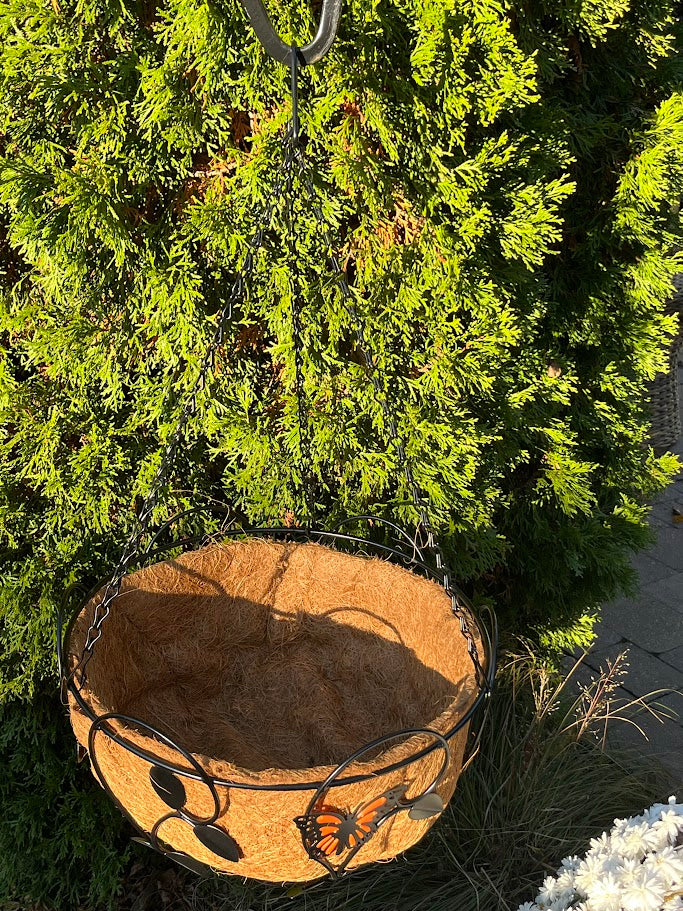 Hanging basket with butterfly design against a green bush background