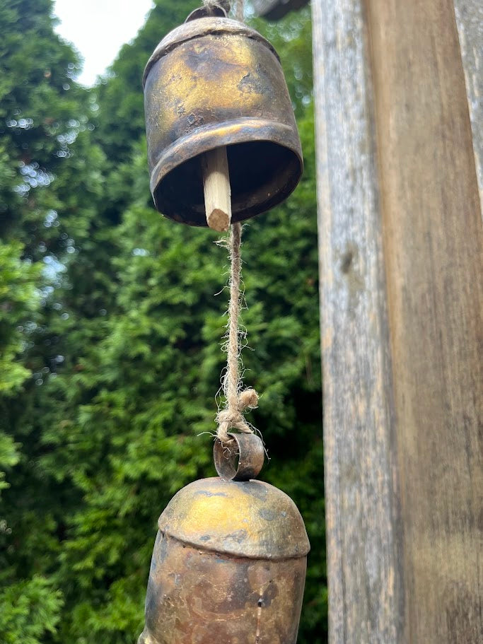 Rustic metal bell hanging on a wooden post with greenery in the background