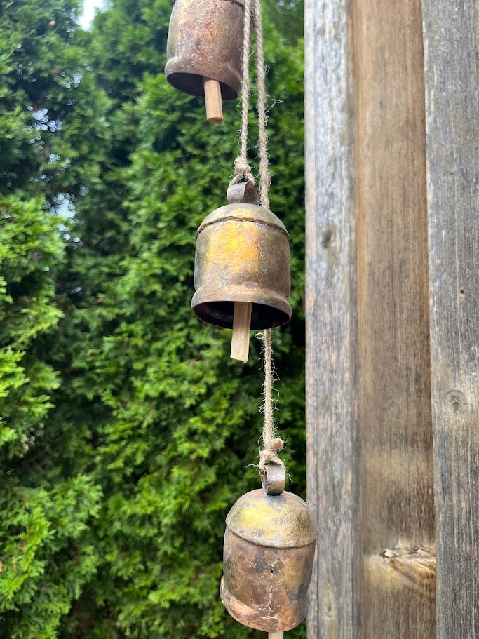 Vintage-style metal bell chime hanging on a wooden post with green foliage in the background