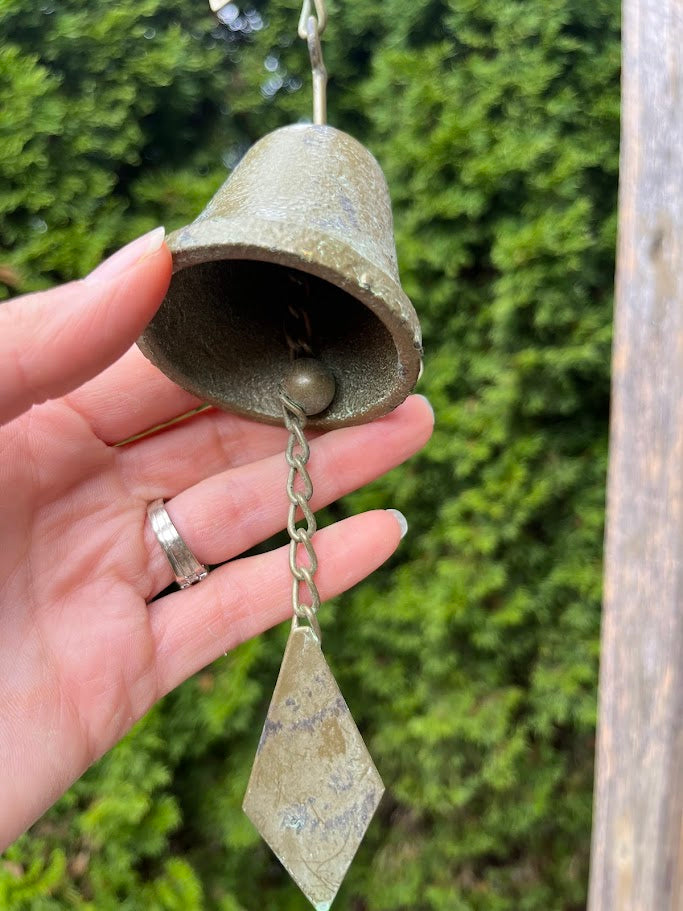 Hand holding a rustic bell with a greenish patina against a blurred natural background