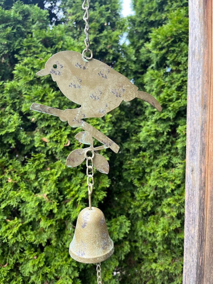 Decorative metal bird with a bell hanging against a green foliage background