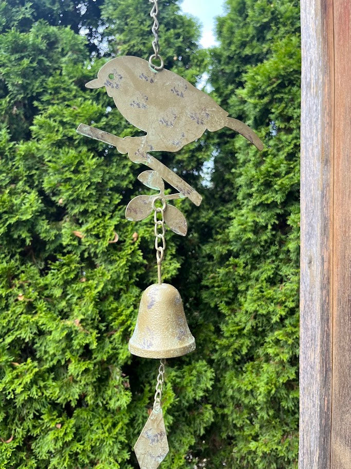 Decorative metal wind chime with bird design against a green foliage background