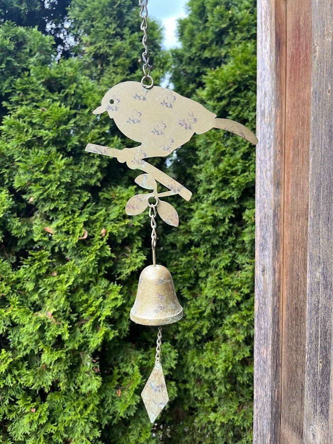 Decorative metal wind chime with bird design against a green foliage background