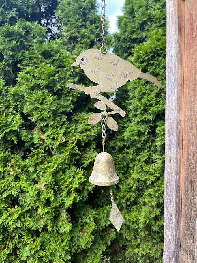 Decorative metal wind chime with bird design against a green foliage background