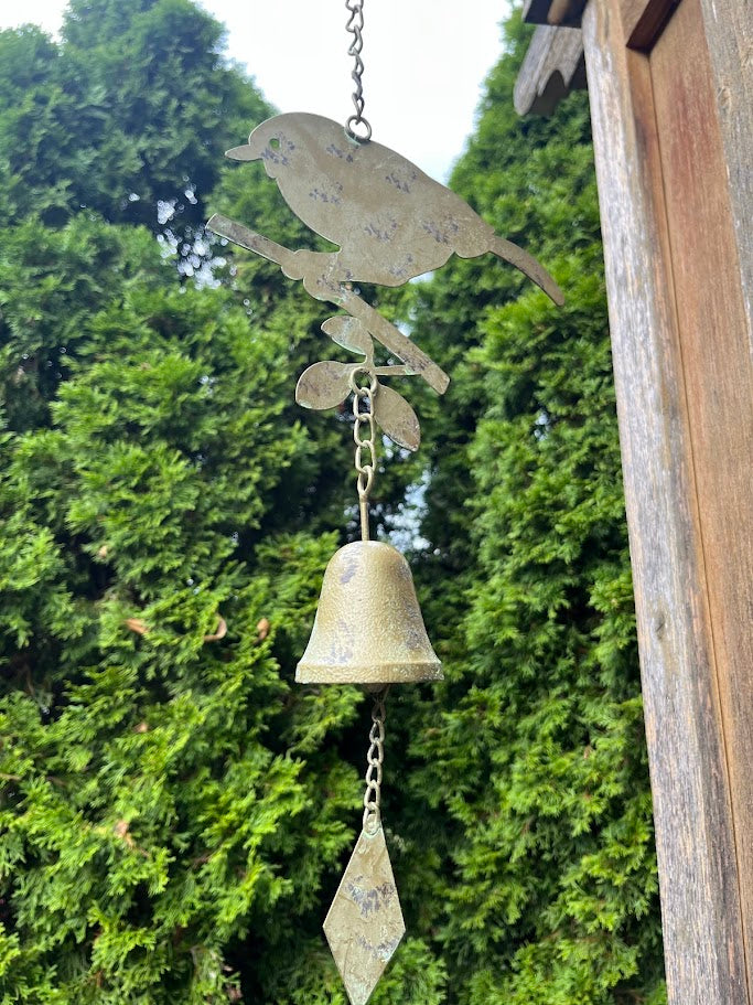 Decorative metal wind chime with bird design against a green foliage background