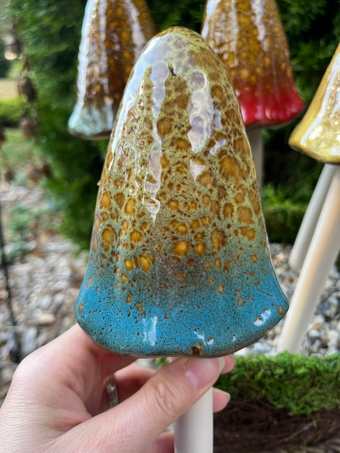 Hand holding a ceramic cone with blue and brown glaze against a garden background