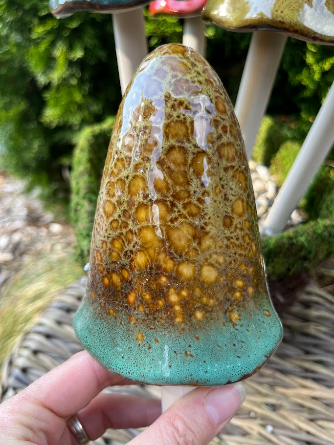 Hand holding a textured ceramic piece with a green base and brown top, against a natural background.