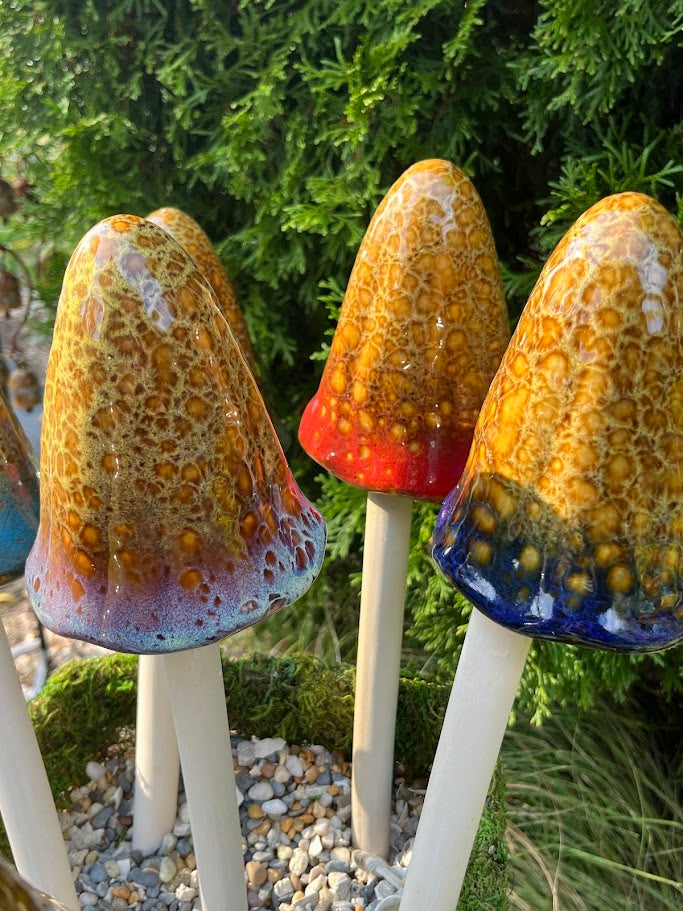 Three colorful ceramic mushroom sculptures on sticks with a natural background.