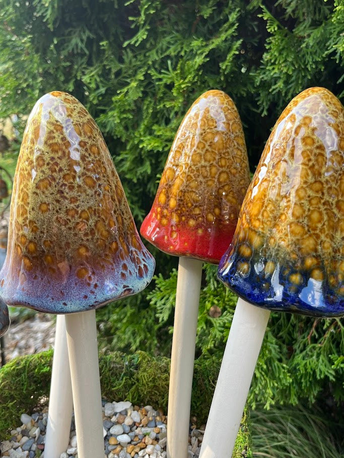 Three ceramic toadstools with colorful caps against a green foliage background
