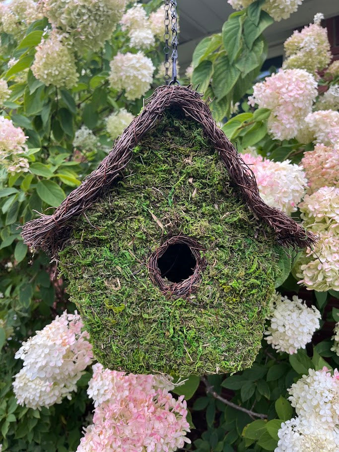Moss-covered birdhouse hanging among white and pink flowers