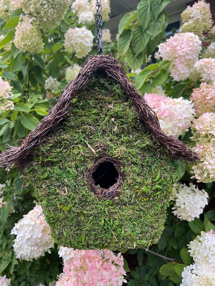Moss-covered birdhouse hanging among white and pink flowers