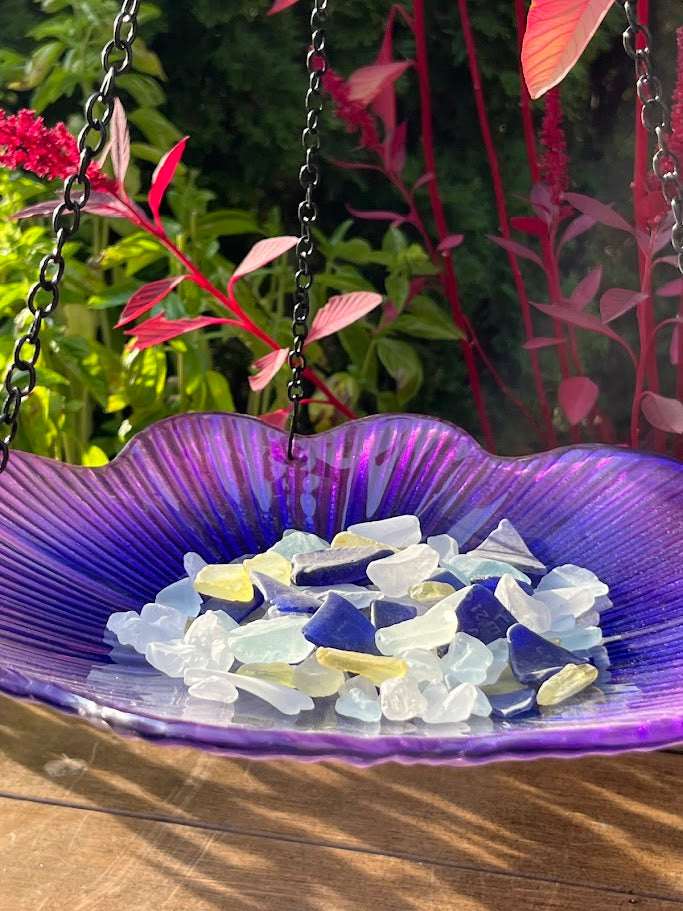 Purple bird bath with colorful pebbles and a garden background