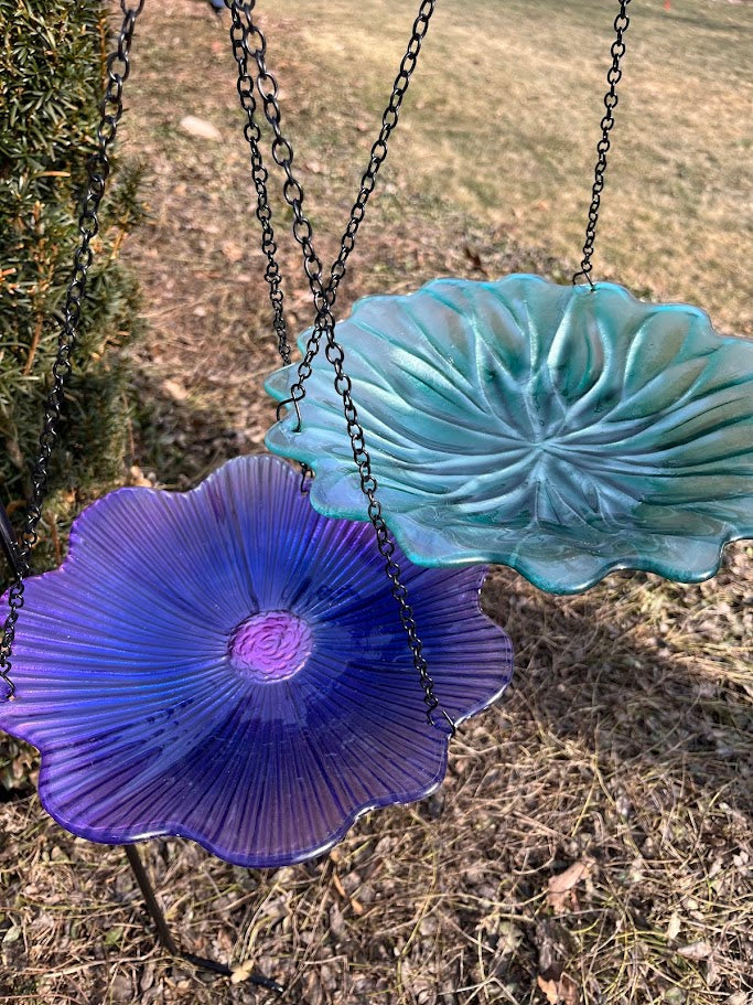 Two colorful glass bird feeders hanging from chains against a natural background.