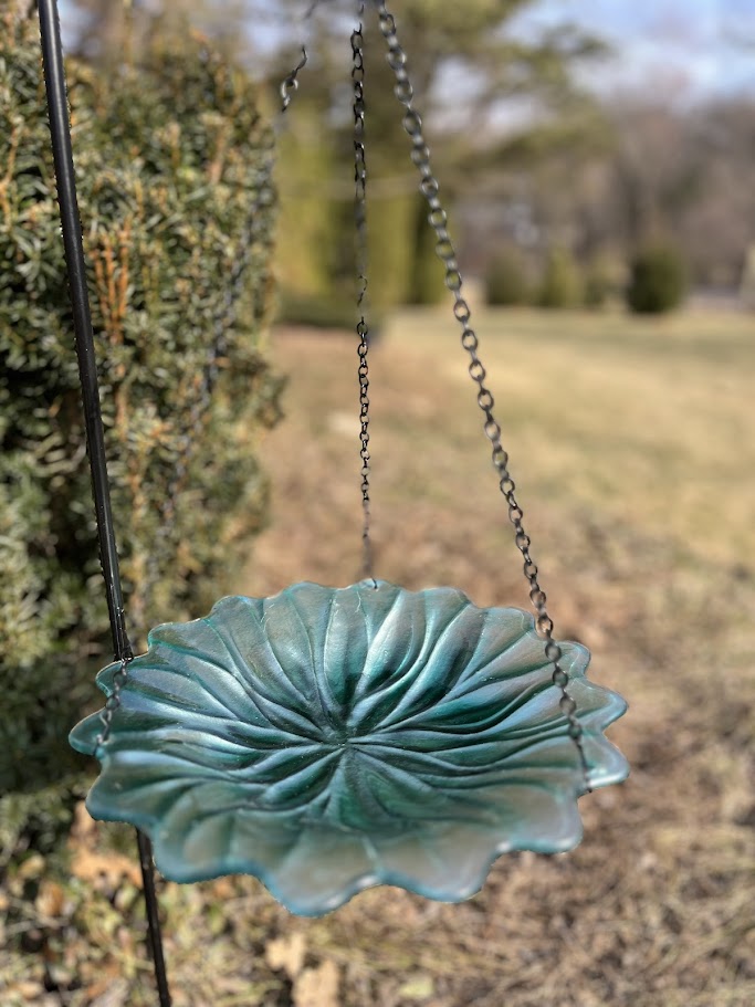 Decorative turquoise bird feeder hanging outdoors with a blurred natural background