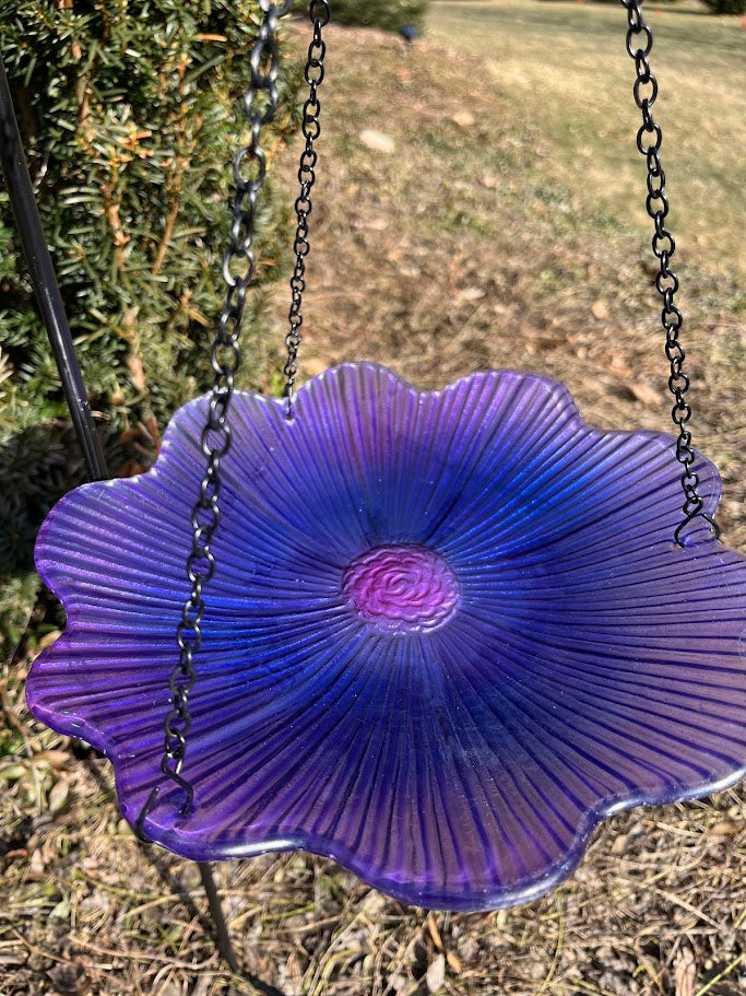 Purple glass bird bath with chains against a natural background