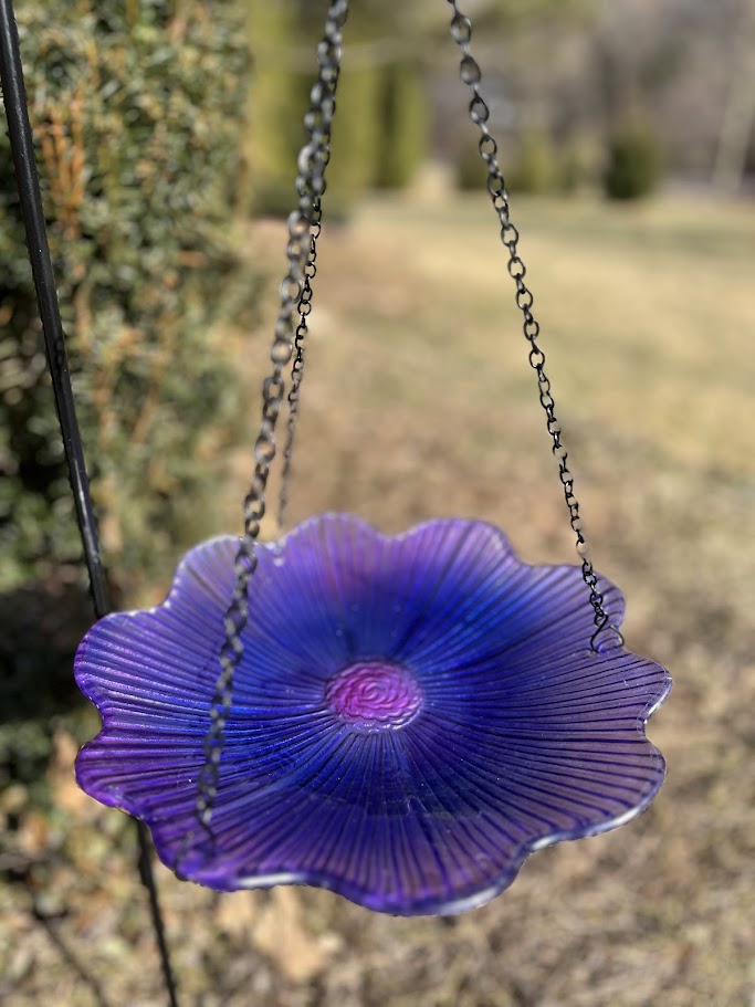 Purple glass bird feeder hanging outdoors with a blurred natural background