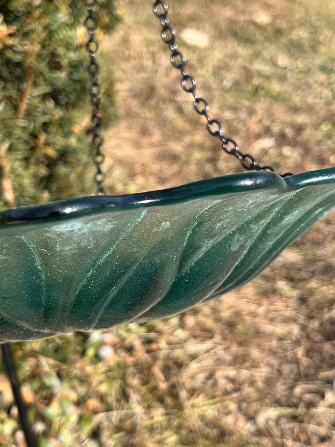 Close-up of a green glass bird bath with a blurred natural background