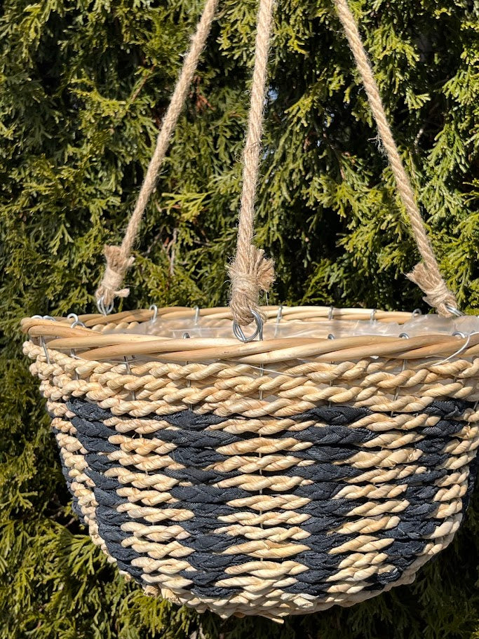 Woven basket with black and beige pattern hanging against a green foliage background
