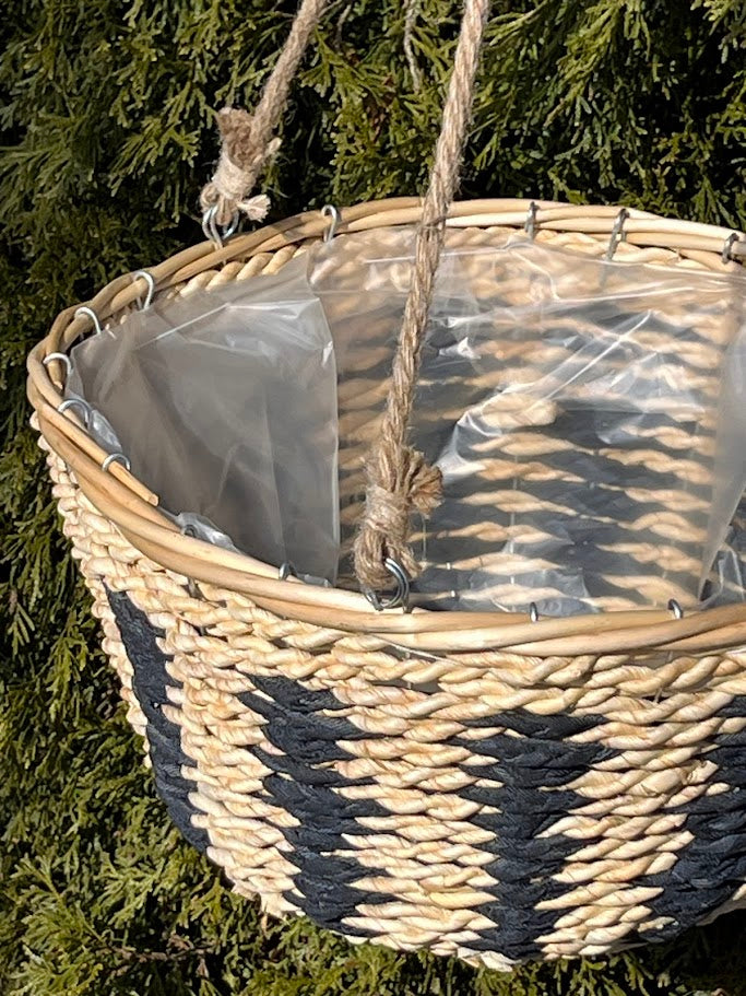 Woven basket with a clear plastic bag inside, hanging against a green leafy background