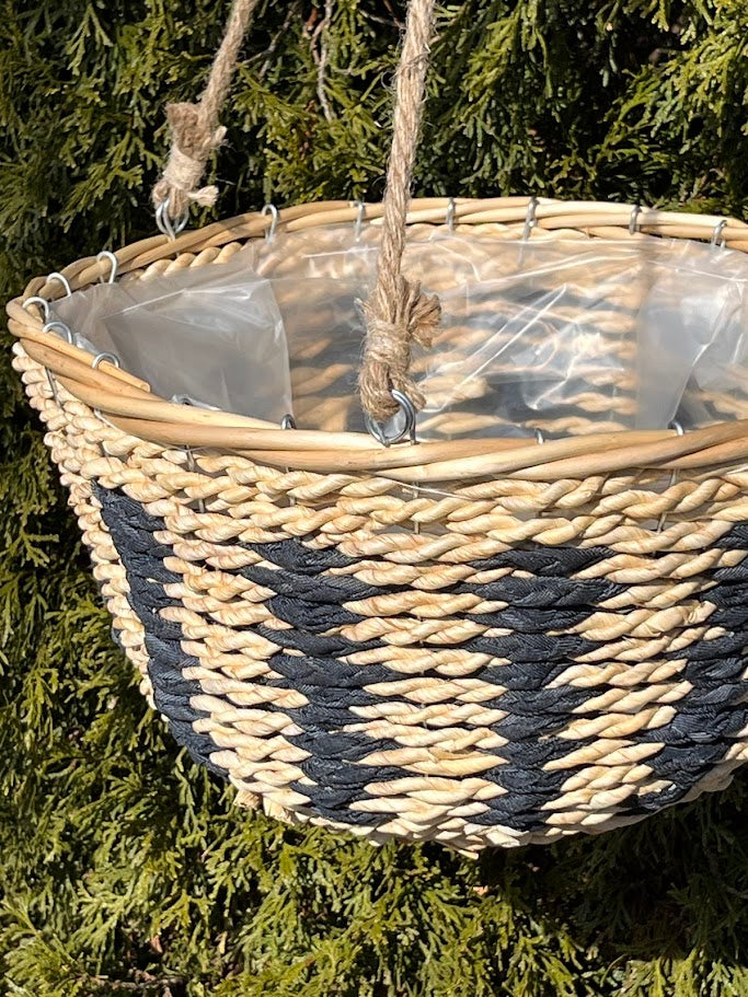 Woven basket with black and white pattern hanging against a green foliage background