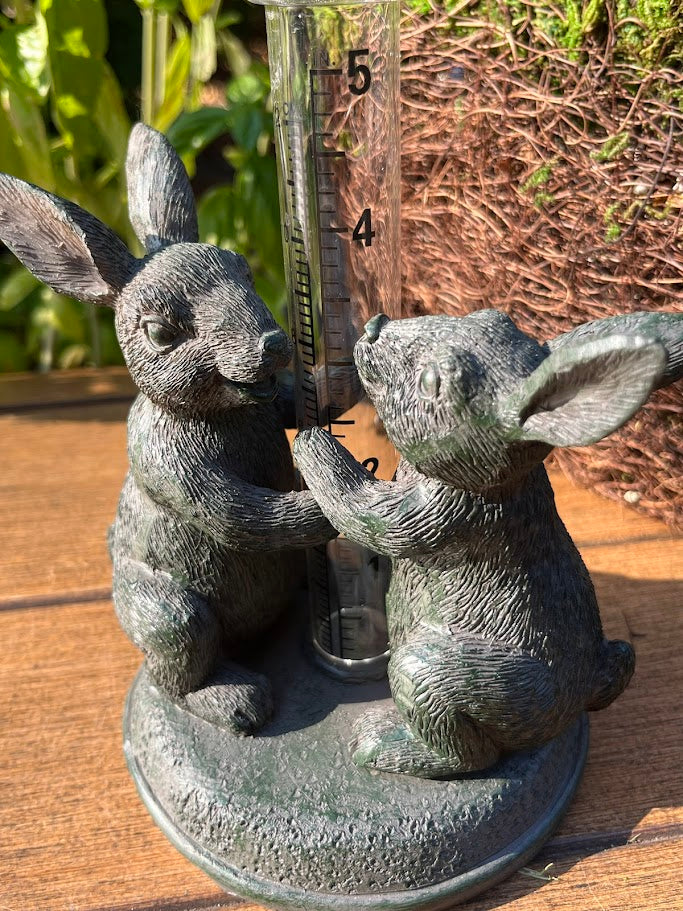 Decorative rain gauge with two rabbit statues on a wooden surface