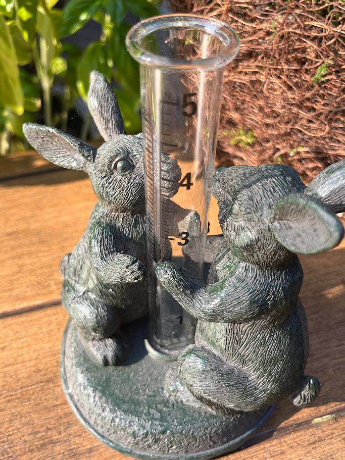 Decorative rain gauge with rabbit sculptures on a wooden surface