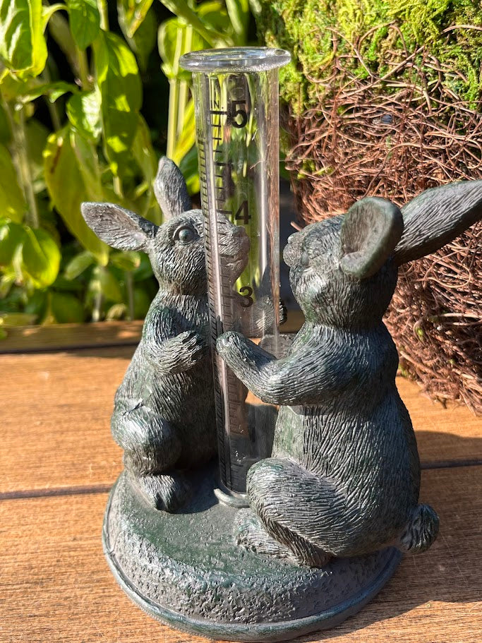 Decorative rain gauge with rabbit sculptures on a wooden surface