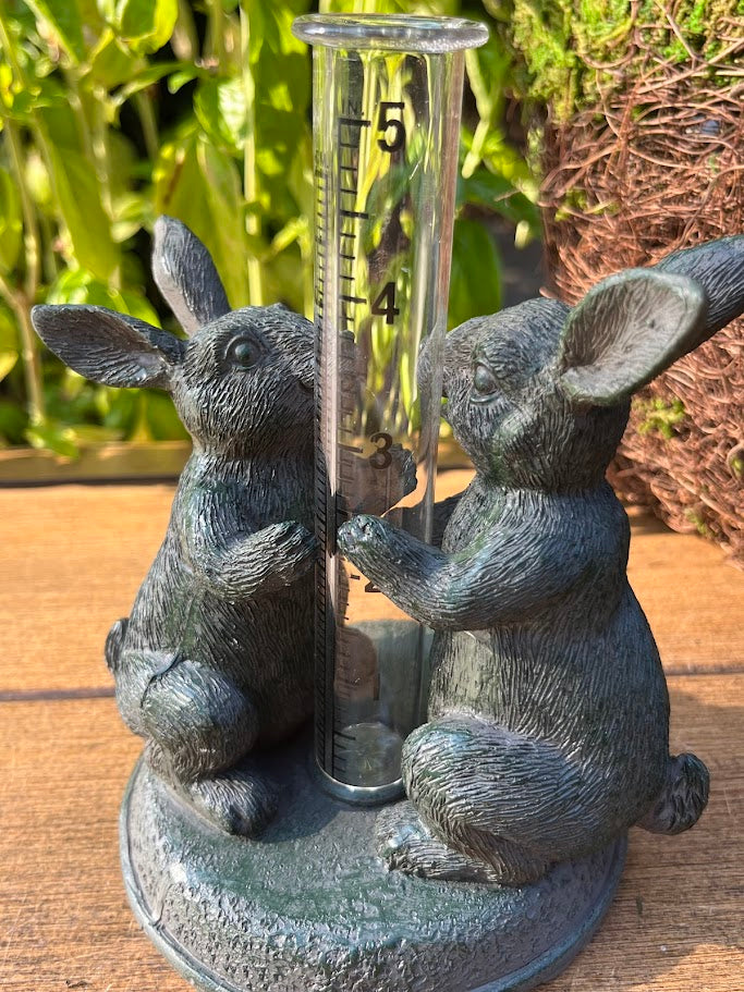 Decorative rain gauge with rabbit sculptures on a wooden surface