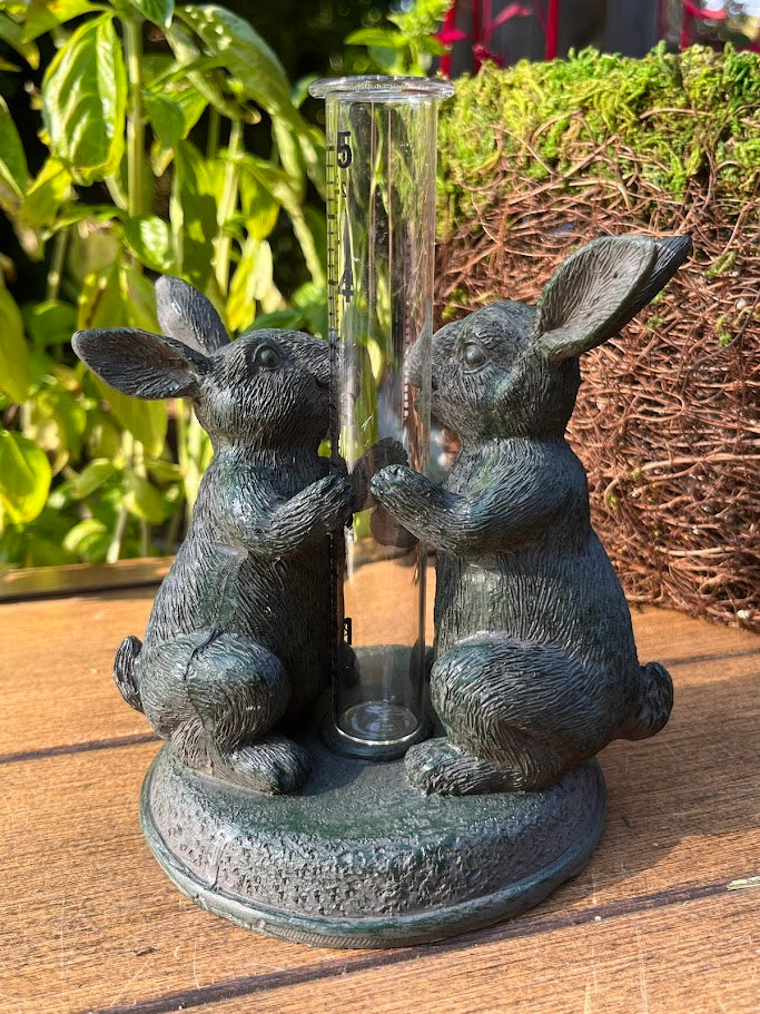 Decorative rain gauge with rabbit sculptures on a wooden surface