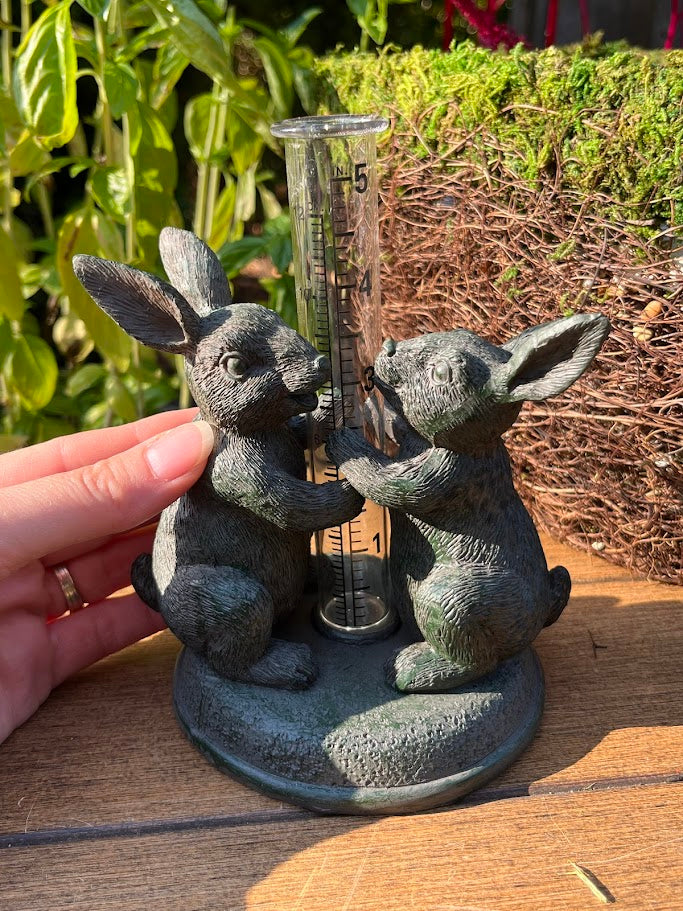 Decorative rain gauge with rabbit sculptures outdoors