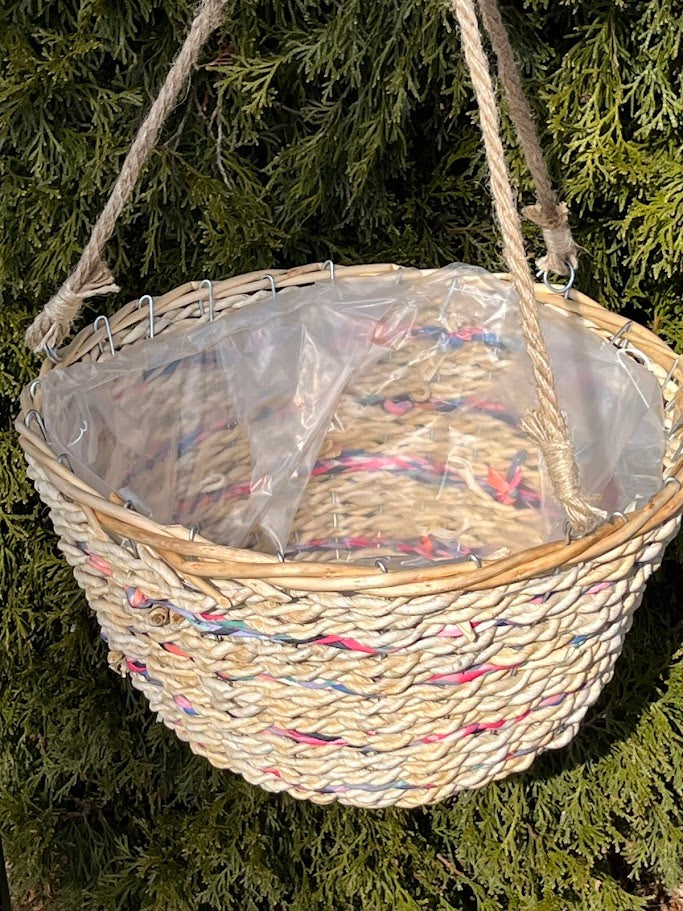 Woven basket with a clear plastic liner hanging against a green leafy background