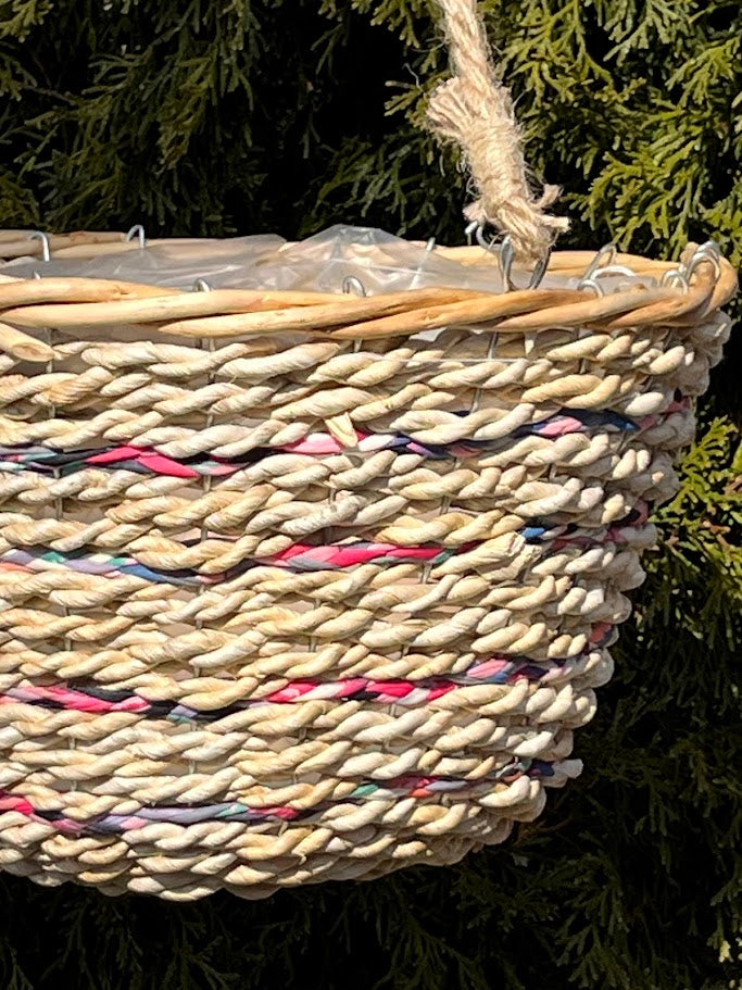 Woven basket with colorful accents hanging against a green leafy background