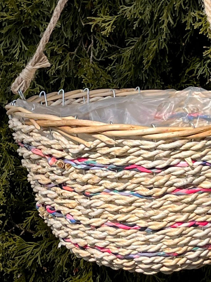 Woven basket with colorful accents hanging against a green leafy background
