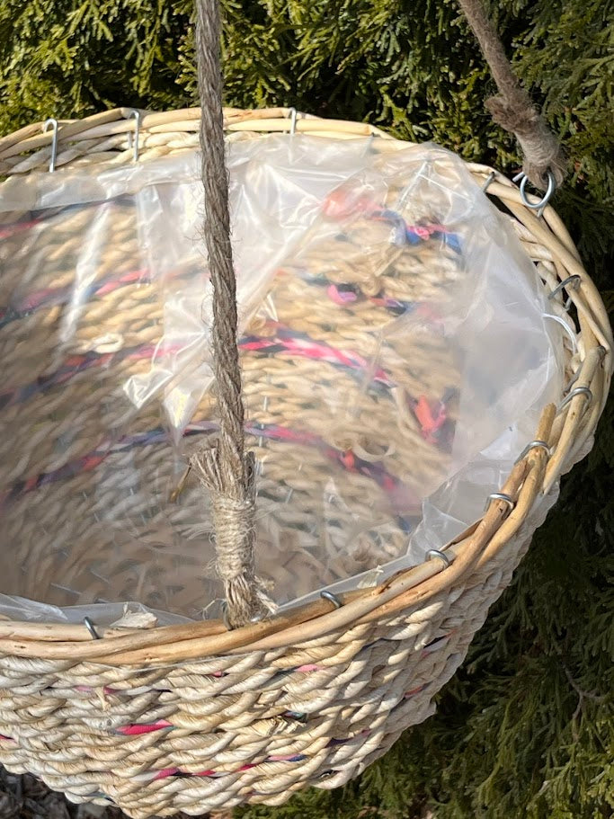 Woven basket with colorful threads inside, hanging against a green background