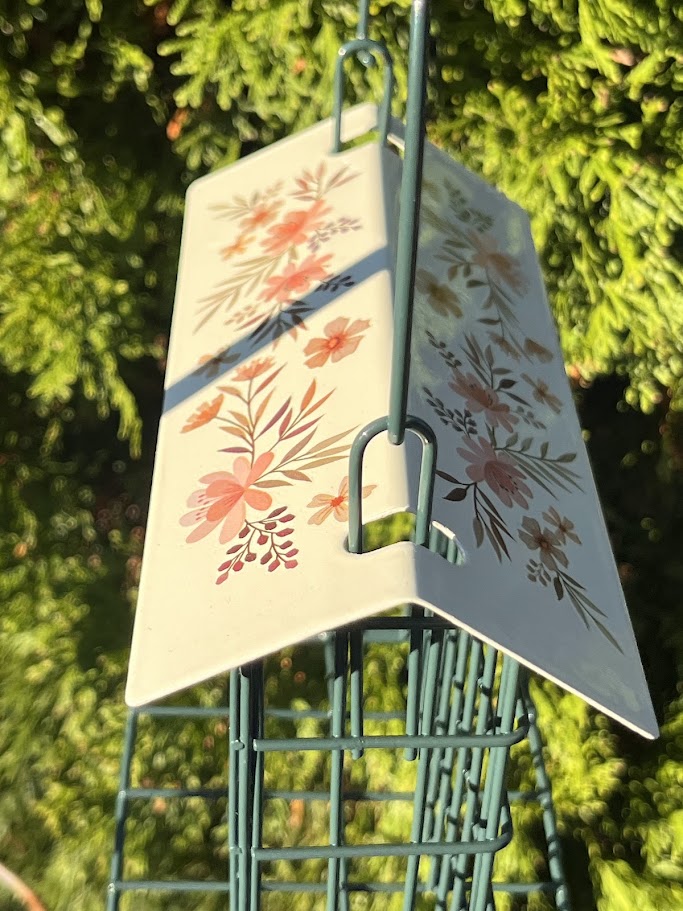 Decorative bird feeder with floral design against a green foliage background