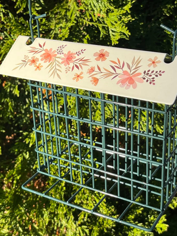 Bird feeder with floral design on top against a green foliage background