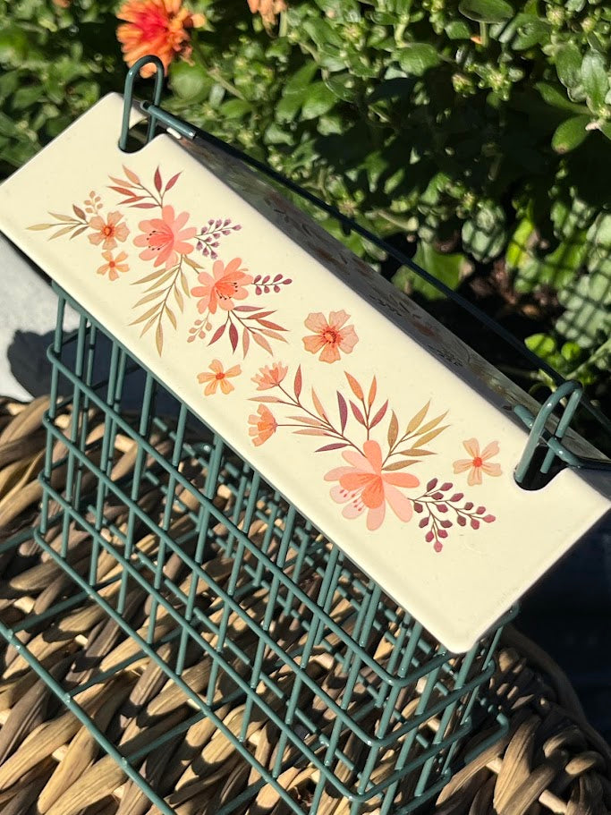Floral design on a rectangular white  bird feeder with green wire basket