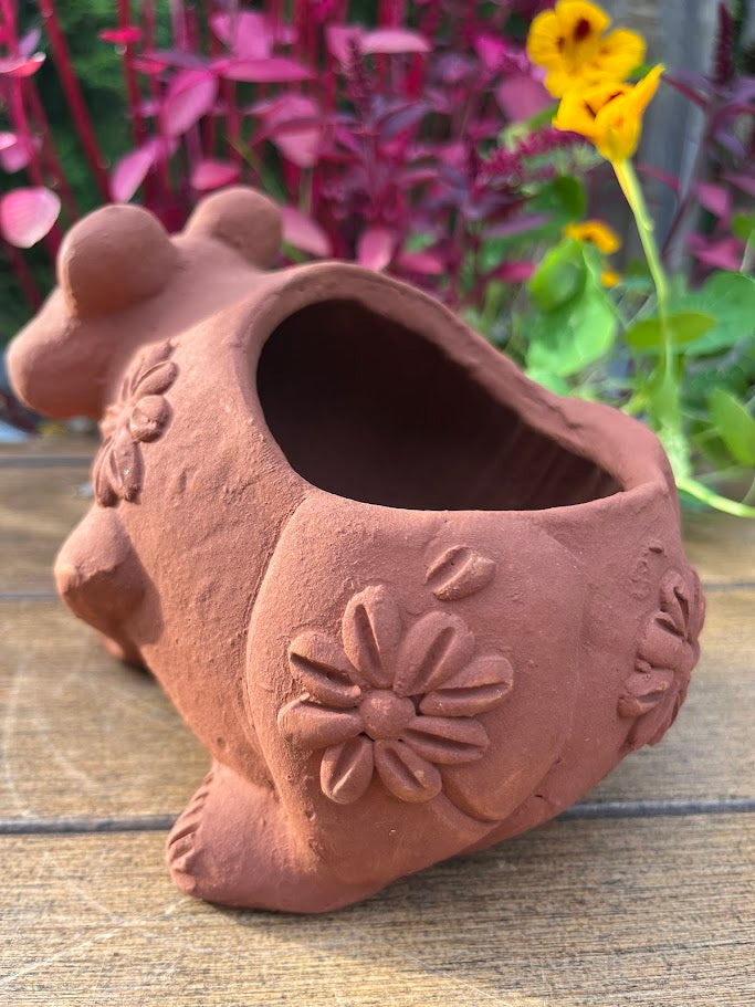 Terracotta pot shaped like a rooster with floral designs on a wooden surface.