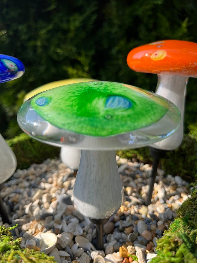 Decorative garden mushroom lights with colorful tops on a pebble-covered ground.