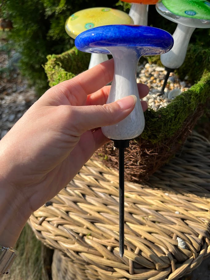 Hand holding a small mushroom-shaped object with a blue cap and white stem, set against a natural background.